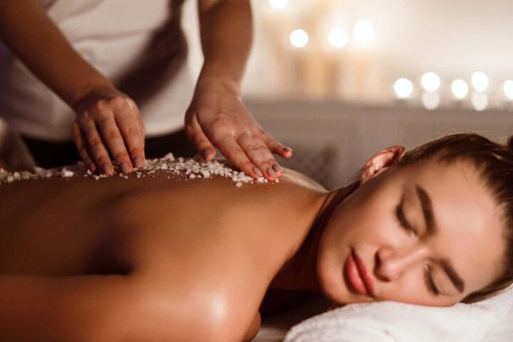 A therapist working a salt scrub across a guest's back